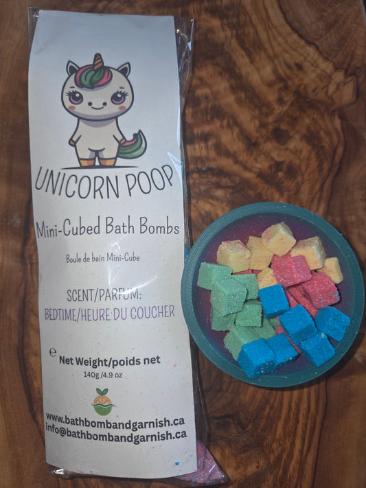 Packaging of Unicorn Poop mini-cubed bath bombs in Bedtime fragrance with colorful bath bombs on a wooden surface to show